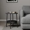 A dark gray side table with a lower shelf is placed next to a gray sofa in a room with gray walls and a wooden floor. Náhled obrázku produktu