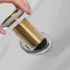 A hand is holding a gold and white drain assembly over a sink drain. Produktbild-Vorschau