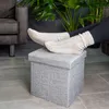 A person's feet wearing socks rest on a gray fabric ottoman in a living room setting. Náhled obrázku produktu