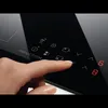 A close-up shot of a finger interacting with the control panel of a black induction cooktop. Voir les images du produit