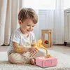 A young child is playing with a pink toy record player on a rug. Produktbild-Vorschau