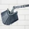 A close-up shot of a gray triangular brush with an adjustable telescopic handle against a white tiled background. Podgląd zdjęcia produktu