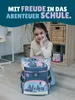 A young girl is sitting on the floor with a school backpack in front of her. The background shows a room with furniture. Produktbild-Vorschau
