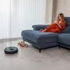 A woman relaxing on a couch while a robot vacuum cleans the floor. Náhled obrázku produktu