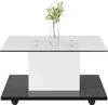 A modern coffee table with a glass top and a white cube-shaped pedestal base, set on a black base with wheels. Voir les images du produit