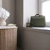 A green toiletry bag sits on a windowsill next to two glasses, with a woven basket and a vase of white flowers in the foreground. Produktbild-Vorschau