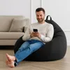 A man is sitting on a black beanbag chair in a living room, looking at his phone. A sofa is visible in the background. Voir les images du produit