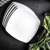 A stack of white square plates on a black surface, with some green vegetables on the side. Náhľad obrázku produktu