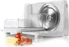 A white electric slicer with a circular blade, positioned on a white surface. In front of the slicer are some slices of cheese, a tomato, and some cured meat. Produktbild-Vorschau