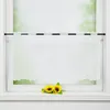 A white sheer curtain with embroidered leaf patterns hangs on a window rod, with two artificial sunflowers placed on the windowsill below. Produktbild-Vorschau