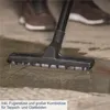 A vacuum cleaner head with brushes is shown cleaning a wet floor. The legs and shoes of a person are visible in the background. Produktbild-Vorschau