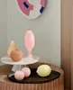 A collection of decorative fruit-shaped candles and a cake stand are displayed on a textured wooden table. Produktbild-Vorschau