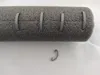A close-up view of a gray foam pipe insulation with several gray clips attached, and one clip lying on the white surface below. Produktbild-Vorschau