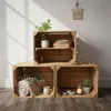 Three wooden crates stacked and arranged as shelving, decorated with plants, books, a rolled blanket, a mug, stones, and a lantern with a candle. Produktbild-Vorschau