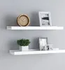Two white shelves mounted on a light gray wall, decorated with a clock, a plant, and picture frames. Anteprima dell’immagine prodotto