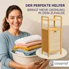 A woman holds a laundry basket filled with folded towels next to a bamboo shelving unit with a laundry basket. Produktbild-Vorschau
