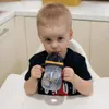 A young child is sitting in a high chair and drinking from a sippy cup. Anteprima dell’immagine prodotto