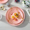 A table setting with pink and gold marble-patterned plates, cutlery, and a small fruit tart. Produktbild-Vorschau