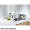 A stainless steel corner sink with a faucet, lemons, and a glass of dessert on a white countertop. Náhled obrázku produktu