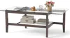 A glass-top coffee table with a wooden frame and a lower shelf, decorated with books, boxes, and a vase of flowers. Anteprima dell’immagine prodotto