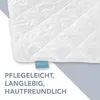 A close-up of a white quilted blanket with a blue tag and text overlay. Produktbild-Vorschau