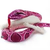 A pink python plush toy is coiled around a white bone-like object. Produktbild-Vorschau