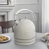 A cream-colored electric kettle with a silver handle and trim sits on a table next to a plate of cookies and a cup of tea. Produktbild-Vorschau