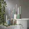 A collection of LED candles in various colors and sizes arranged on a white surface with ivy vines. Podgląd zdjęcia produktu
