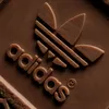 A close-up, embossed view of the Adidas logo and wordmark on a brown textured surface. Náhled obrázku produktu