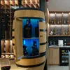 A wooden barrel-shaped bar with bottles of alcohol displayed inside, illuminated by blue LED lights. Shelves with more bottles are visible in the background. Produktbild-Vorschau