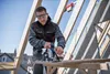 A construction worker is using a circular saw on a wooden beam on a roof. Anteprima dell’immagine prodotto