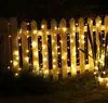 String lights are draped over a white picket fence at night, illuminating the garden. Produktbild-Vorschau