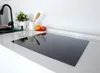 A modern kitchen countertop with a black induction hob, a sink with a black faucet, and a small bowl of fruit. Anteprima dell’immagine prodotto