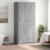 A gray wood-effect wardrobe is shown in a room with a painting on the wall and a bed in the background. Produktbild-Vorschau