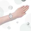 A person's arm wearing a watch and a ring, with abstract circles in the background. Produktbild-Vorschau