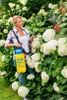 A woman is using a garden sprayer on a bush with white flowers. Produktbild-Vorschau