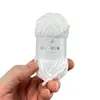 A hand holding a ball of white yarn with a label. Produktbild-Vorschau