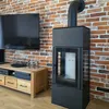 A modern living room with a brick wall, a television, a media console, and a black wood-burning stove. Produktbild-Vorschau