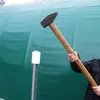 A person is holding a large sledgehammer, aiming it at a white cylindrical object on a metal pole, with a large green tent-like structure in the background. Voir les images du produit