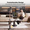 A woman is sitting on a couch with two small dogs, while a cordless vacuum cleaner stands upright in the foreground. Produktbild-Vorschau