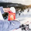 Hands holding a package of foot warmers in a snowy mountain environment with skis in the background. Voir les images du produit