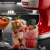 A red and white ice crusher machine is shown in the background, with three glasses of slushy drinks in the foreground, garnished with fruit and mint. Náhľad obrázku produktu