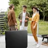 Three people are standing around a black folding table outdoors, appearing to be at a party or gathering. Náhľad obrázku produktu