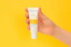A hand holding a tube of Bioderma sunscreen against a bright yellow background. Náhled obrázku produktu