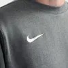 A close-up shot of a dark grey Nike pullover with the Nike logo. Produktbild-Vorschau