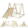 A wooden indoor playground set with multiple activity stations, including a slide, swing, climbing net, and climbing wall with colorful holds. The image also shows smaller inset images of the playground in different configurations. Podgląd zdjęcia produktu
