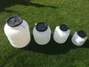 Four white plastic containers of varying sizes with black lids are arranged on a green grassy surface. Produktbild-Vorschau