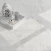 A white fluffy rug with a white tray containing a white lantern, a gray candle, and a white decorative apple. Produktbild-Vorschau