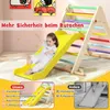 A young child is sliding down a yellow slide attached to a wooden climbing triangle. The image is overlaid with text and graphics highlighting product features. Produktbild-Vorschau