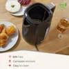 A black electric kettle is shown on a wooden table next to breakfast items like croissants, a bagel with cream cheese, and jam, along with a glass of tea. Podgląd zdjęcia produktu
